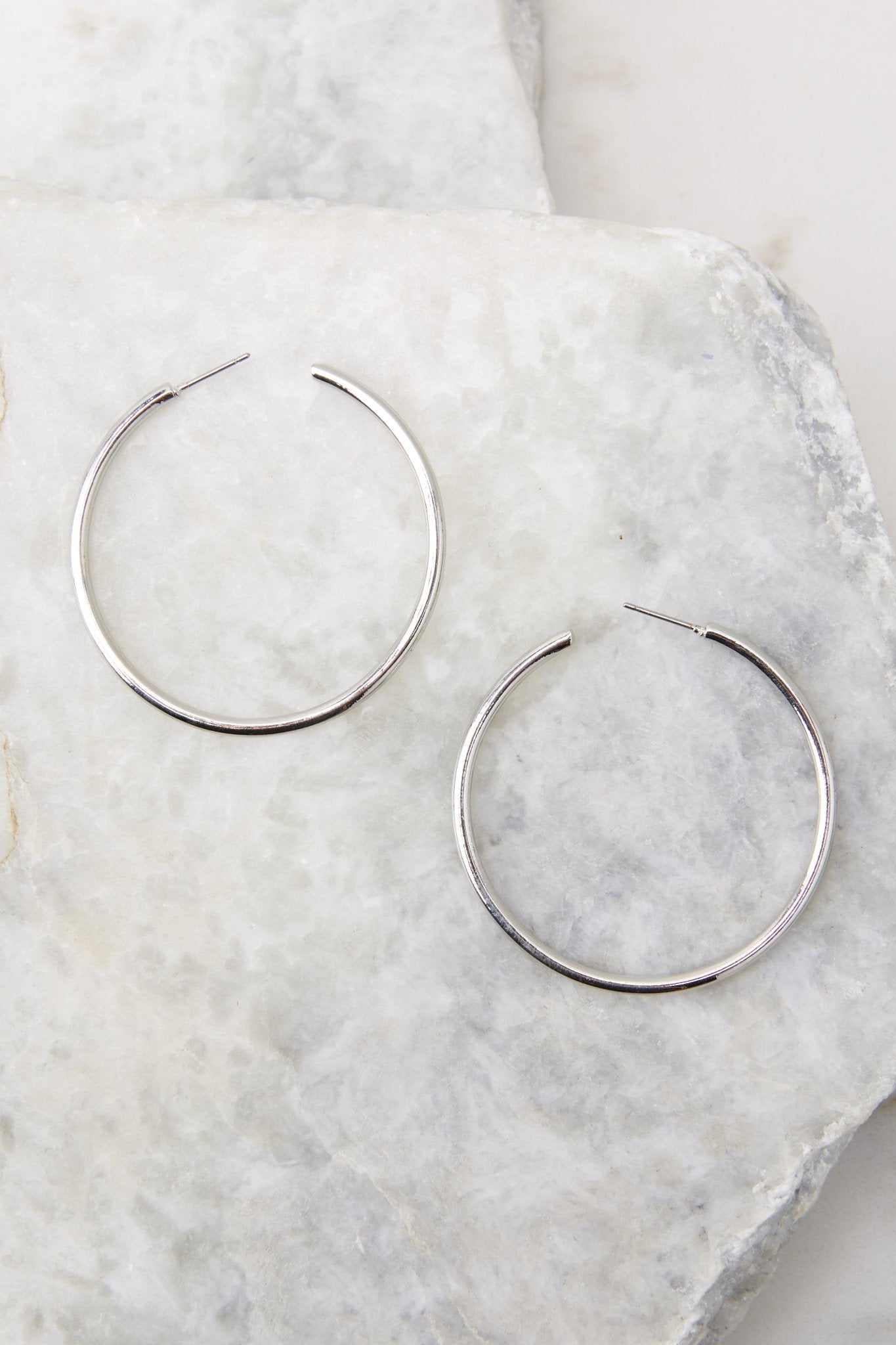 Detailed view of hoop earrings that feature a thin lightweight design, silver hardware, and a post secure backing.