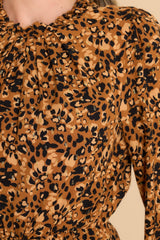 Close up view of this dress that features a high neckline with ruffle detailing, a keyhole cutout at the back of the neck with a button closure, long sleeves with elastic cuffs, an elastic waistband, and gold metallic detailing throughout. 