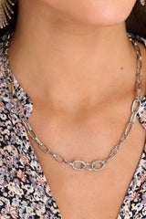 Model is shown wearing necklace that features an alternating silver chain link pattern with the links varying in shape and texture and a lobster claw clasp.