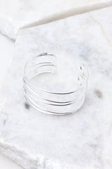 An elegant silver cuff bracelet showcased on a polished marble surface.