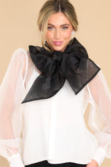 Front view of  this top that features a high neckline with an oversized bow detail, a sheer puff sleeves with buttons at the cuffs, and is lined with a white tank.
