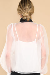 Back view of  this top that features a high neckline with an oversized bow detail, a sheer puff sleeves with buttons at the cuffs, and is lined with a white tank.