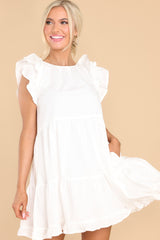 Front view of this dress that features a round neckline, flutter sleeves, a functional button in the back with a small keyhole cutout below, functional pockets at the hips, and a flowy tiered skirt.