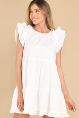 This all white dress features a round neckline, flutter sleeves, a functional button in the back with a small keyhole cutout below, functional pockets at the hips, and a flowy tiered skirt.