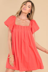 This orange dress features a square neckline, puff sleeves, a cross back with an adjustable tie, and a relaxed/oversized fit.