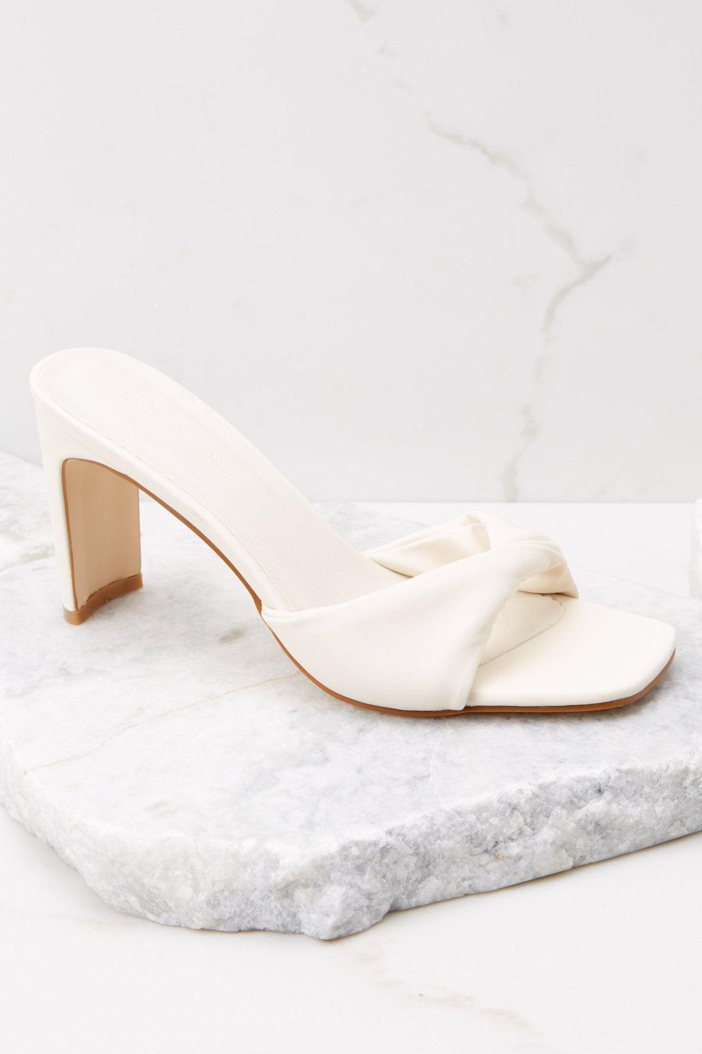 Outer-side view of  these heels that feature a square toe, a twisted strap across the top of the foot, a thin straight heel, and a slip on design.