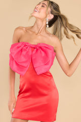 Front view of this dress that features a strapless neckline with a non-slip rubber strip, a zipper in the back, a large bow detail at the center of the bust, boning in the bust section, and a satin feel.
