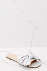 Outer-side view of these sandals that feature a silver bow and a flat sole.