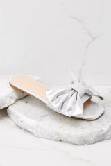 These silver sandals feature a silver bow and a flat sole.