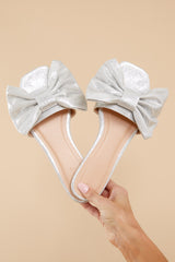 Top view of these sandals that feature a silver bow and a flat sole.