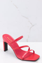 Close up view of  these heels that feature a square toe, red insole, three straps, black soles, and a wide heel.