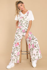 These ivory floral overalls feature a square neckline, adjustable straps, bib overall buckles, a pocket on the front of the bust with a functional zipper, two functional side pockets, two functional back pockets, three functional buttons along either hip, and flared pant legs.