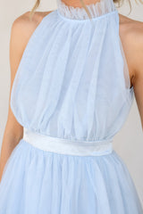 Close up view of this dress that features a high neckline with ruffle detailing, a button closure at the back of the neck with a keyhole cutout, a zipper in the back, and a long tiered skirt.