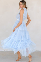 This light blue dress features a high neckline with ruffle detailing, a button closure at the back of the neck with a keyhole cutout, a zipper in the back, and a long tiered skirt.