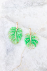 Close up view of these tropical earrings that feature a leaf design with gold flecks set into acrylic, and gold hardware.