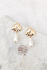 These earrings feature a seashell stud base, secure post backing, and oval, pearl dangles compared to a quarter for actual size. 