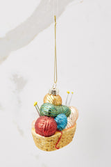 Top view of this ornament that features faux balls of yarn and knitting needles with gold sparkle detailing.
