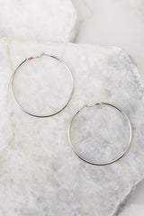 Full view of these hoop earrings that feature a thin lightweight design, a medium size, silver hardware, and a post secure backing.