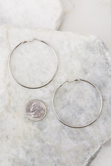 Close up view of these hoop earrings that feature a thin lightweight design, a medium size, silver hardware, and a post secure backing.