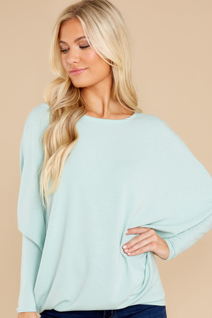 This seafoam colored pull over top features a round neckline, long dolman sleeves, and a slight high low hem line.