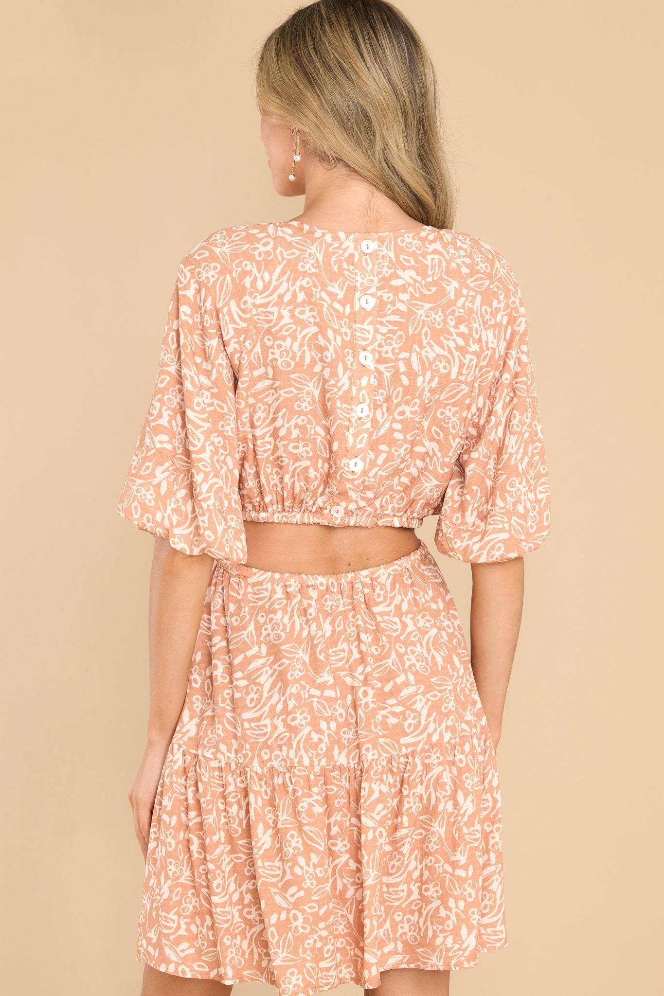 Back view of this dress that features a round neckline, functional buttons down the back, puff sleeves with elastic cuffs, a cutout around the waist with two elastic bands, and a flowy skirt.