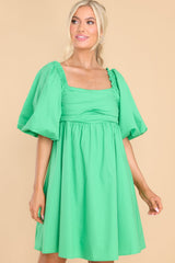 Front view of  this dress that features a square neckline, puff sleeves with elastic cuffs, adjustable self tie over an open back, pleated detail over bust, and flowy skirt.