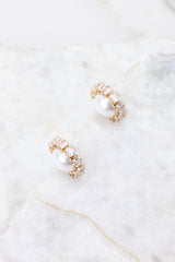 Overhead marble shot of earrings that feature a small rhinestone hoop design, a pearl in the center of the hoop, gold hardware, and a secure post backing.