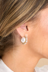 Model shown wearing earrings that feature a small rhinestone hoop design, a pearl in the center of the hoop, gold hardware, and a secure post backing.