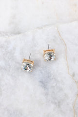Overhead marble shot of gold earrings that feature square rhinestone studs. 
