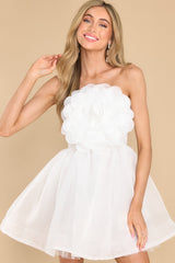 Front view of this dress that features a strapless neckline, a rubber non-slip band around the top of the bust, a smocked section and functional zipper in the back of the bust, a three-dimensional flower detail on the front of the bust, an elastic waistband, and a structured bottom hemline.