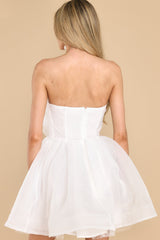 Back view of this dress that features a strapless neckline, a rubber non-slip band around the top of the bust, a smocked section and functional zipper in the back of the bust, a three-dimensional flower detail on the front of the bust, an elastic waistband, and a structured bottom hemline.