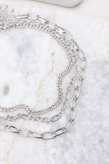 Detailed view of silver necklace stack that features three separate chain necklaces with various lengths and link sizes secured by lobster-claw clasps.