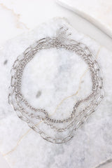 Overhead close-up view of silver necklace stack that features three separate chain necklaces with various lengths and link sizes secured by lobster-claw clasps.